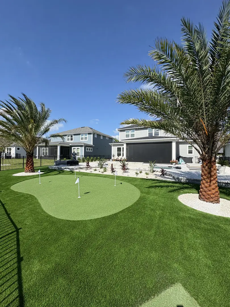 Artificial turf lawn and putting green with date palms leading to a paver pool deck