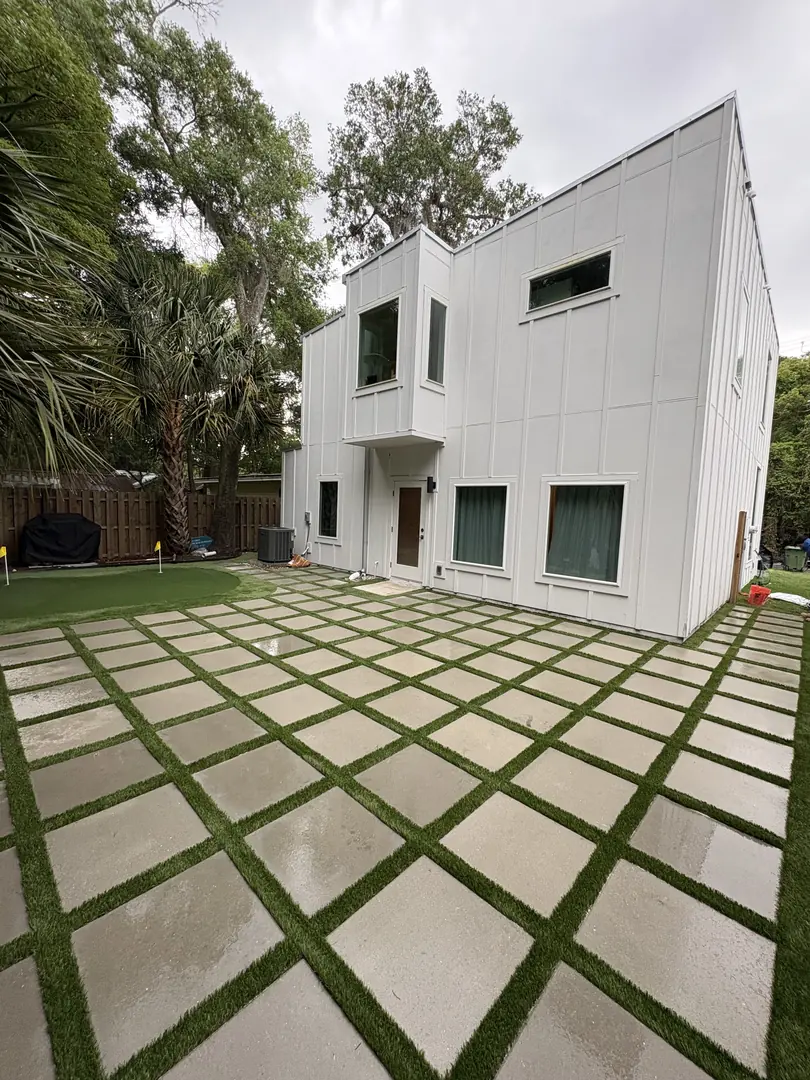 Large-format concrete pavers set with artificial turf joints forming a grid patio at a modern home