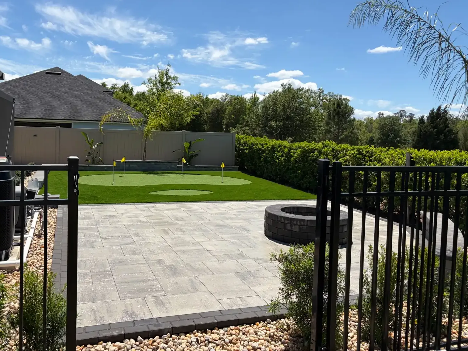 Backyard landscape design with artificial putting green, paver patio and stone fire pit in St. Johns County, FL
